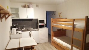 Una habitación compacta con kitchenette, una litera, una mesita y una silla.