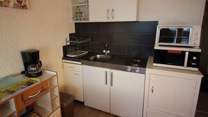 Una cocina compacta con gabinetes blancos, una encimera negra, una cafetera, un microondas y un lavamanos pequeño.