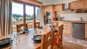 A modern kitchen with wooden cabinets, a dining table set for six, and a view of the outdoors. - Stunning Renovated Mountain-Style 2BR+Cabin Apt near Village Center, Sleeps 6 (Les Gets)