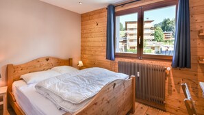 A wooden-paneled bedroom with a bed, a window with curtains, a radiator, and a view of buildings outside. - Stunning Renovated Mountain-Style 2BR+Cabin Apt near Village Center, Sleeps 6 (Les Gets)