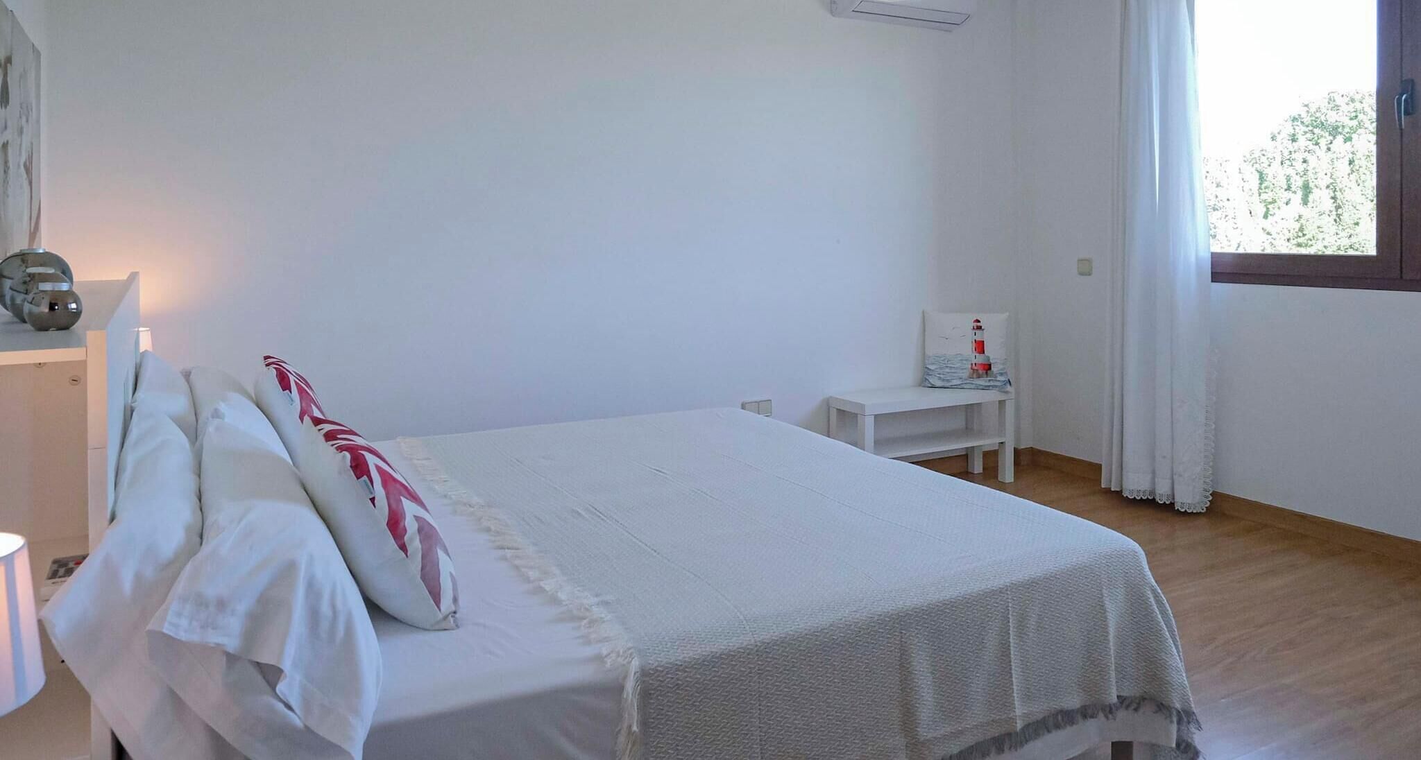 A clean, minimalistic bedroom with a bed, bedside table, and a window with curtains.