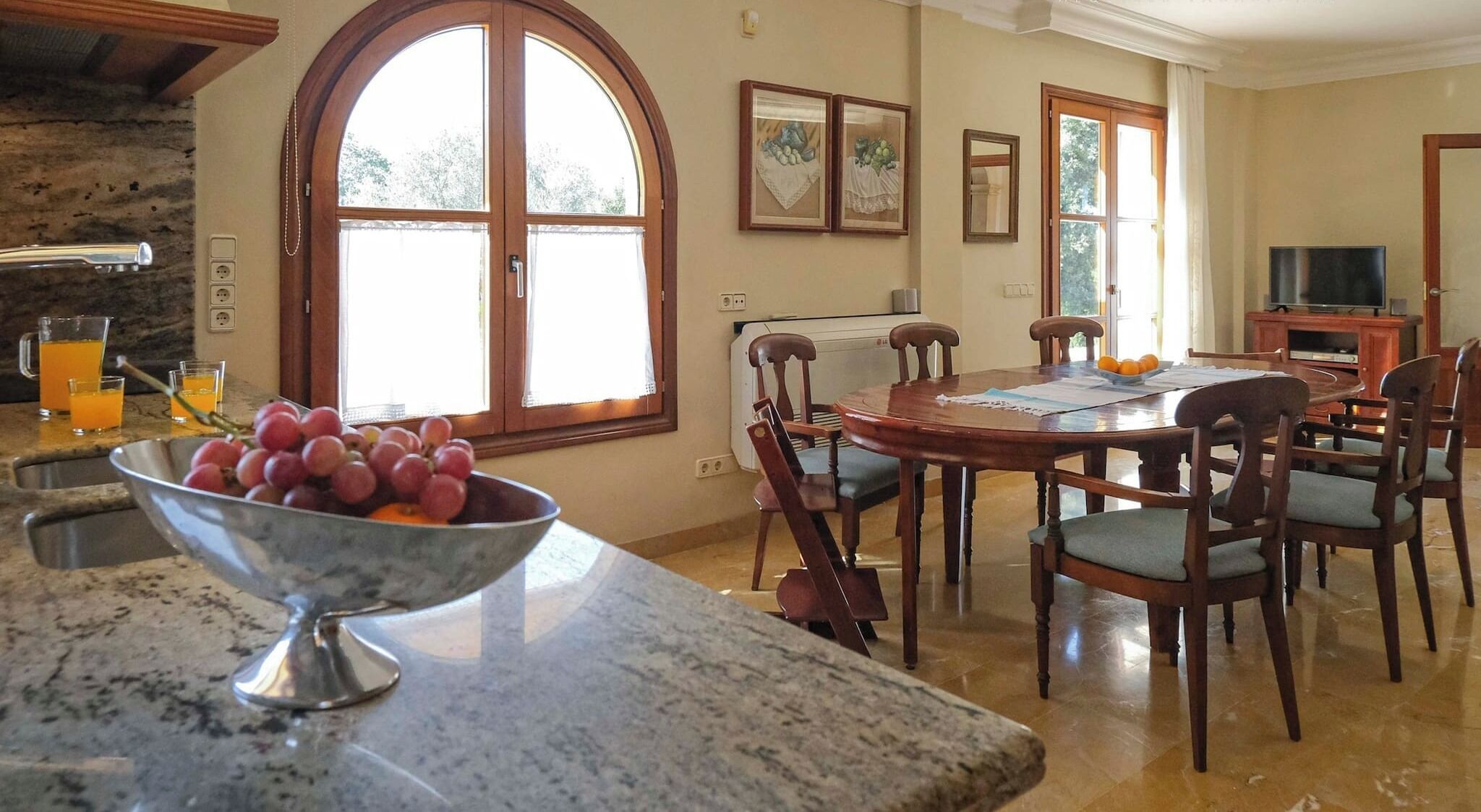 A dining area with a large table, chairs, and a bowl of fruit on the counter.