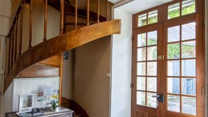 Uma escadaria de madeira com design curvo que leva a um patamar. Uma porta de madeira com painéis de vidro é visível à direita.