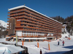 Um hotel com vários andares, varandas, um teleférico e uma paisagem coberta de neve.