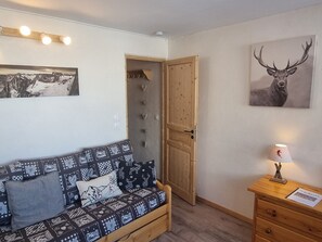 A cozy room with a patterned sofa, a wooden door, a wall-mounted lamp, and a framed deer picture.