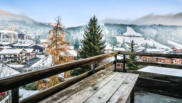 Une terrasse en bois offrant une vue sur une ville enneigée et des montagnes.