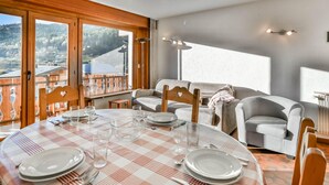 Een eetgedeelte met een ronde tafel voor vier personen, een bank en uitzicht op een bergachtig landschap door grote ramen.