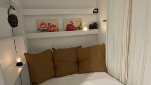 Camera da letto con un letto, cuscini marroni, un comodino con una lampada e mensole a parete con dipinti floreali.