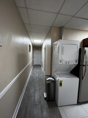 A laundry room with a washing machine, dryer, and trash bin.