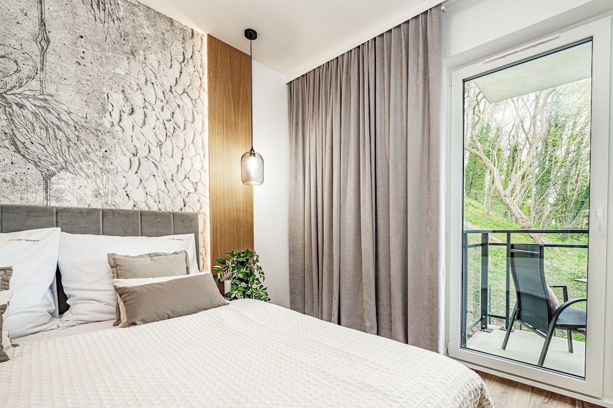 Un dormitorio con una cama grande, una pared de mármol, un panel de madera, una lámpara colgante y un balcón con mesa y sillas.