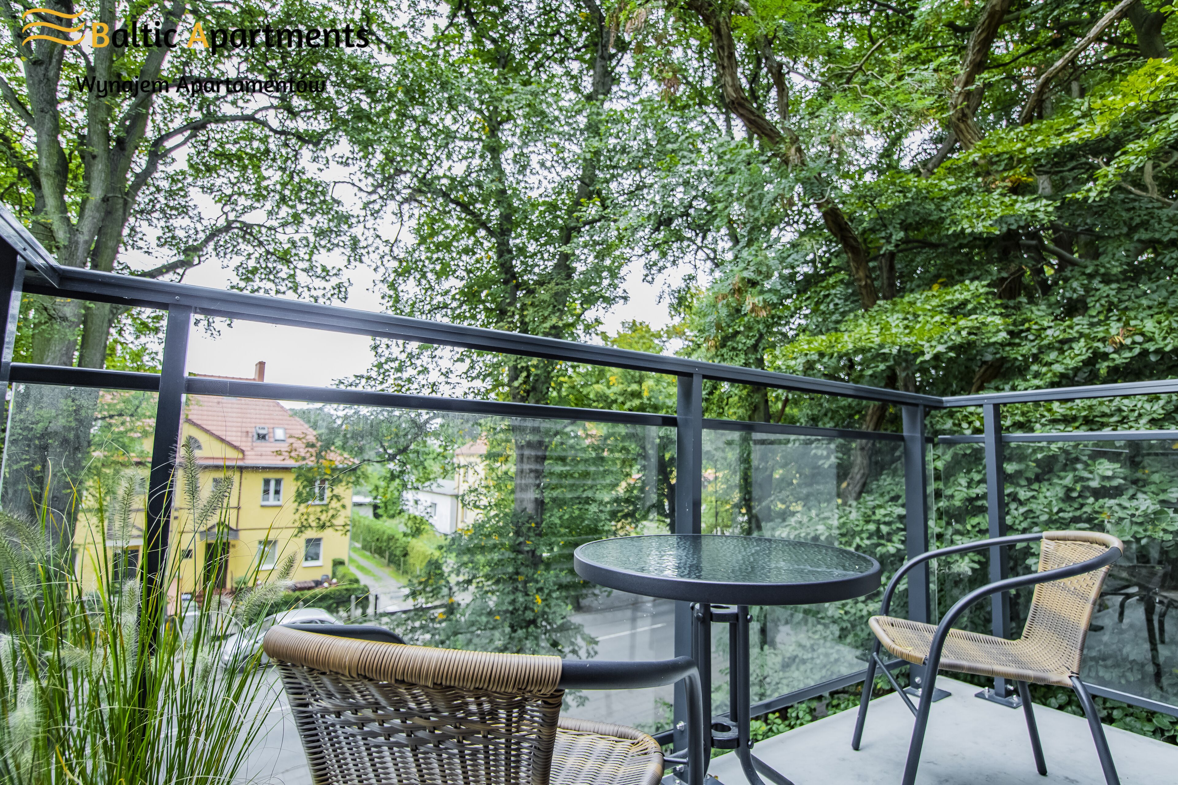 Ein Balkon mit Korbstühlen und einem Glastisch, mit Blick auf eine Straße und Grünflächen.