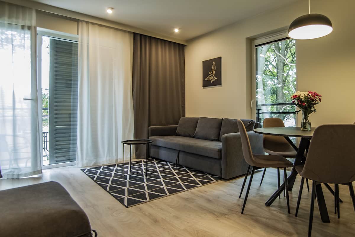 Una sala moderna con un sofá, una mesa de comedor con sillas, una mesita auxiliar y una ventana con cortinas.