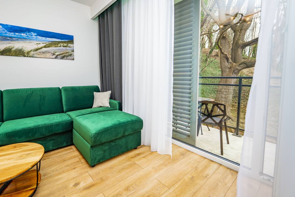 Un sofá verde, una mesa de centro de madera y un cuadro de una escena de playa.
