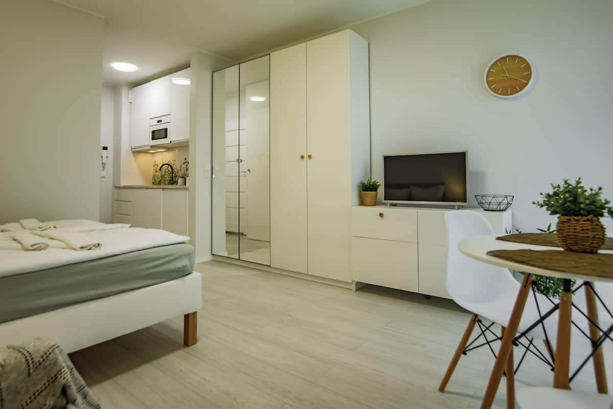 Un dormitorio moderno con cama, televisor, mesa de comedor y una kitchenette al fondo.