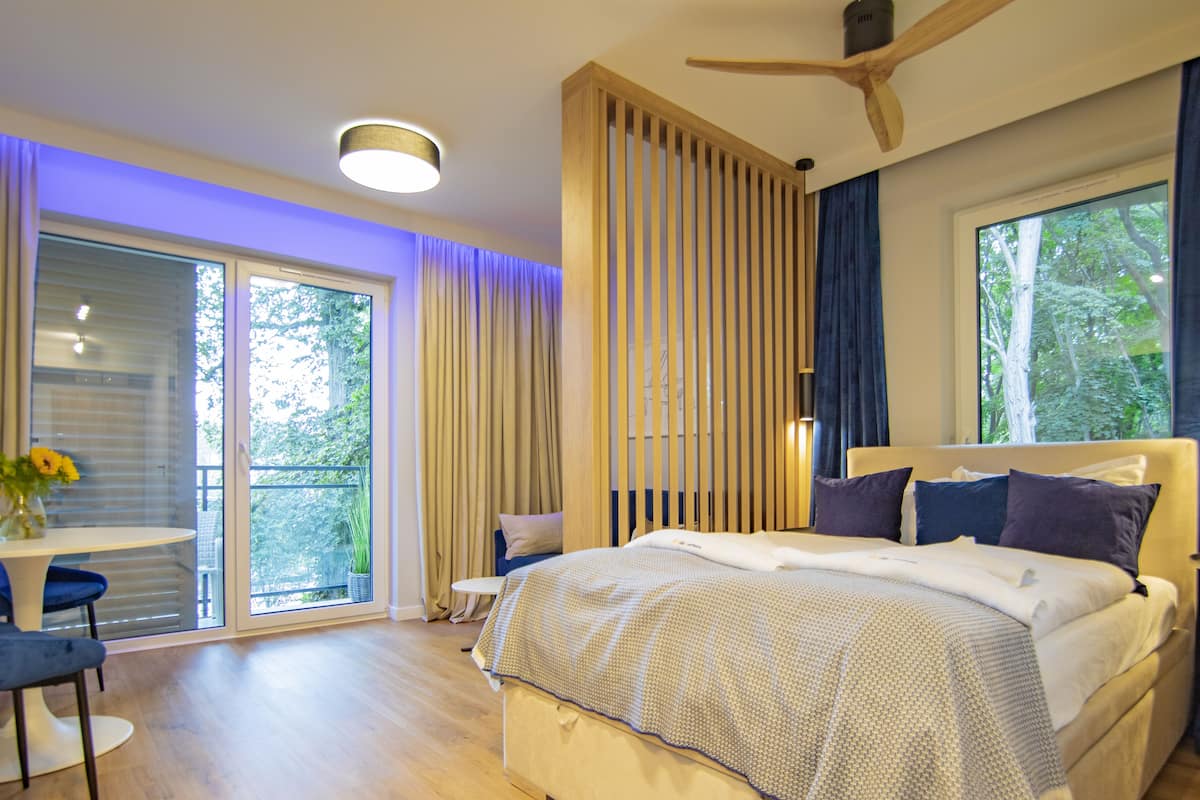 Un dormitorio moderno con una cama grande, ventilador de techo y vistas a árboles a través de las ventanas.