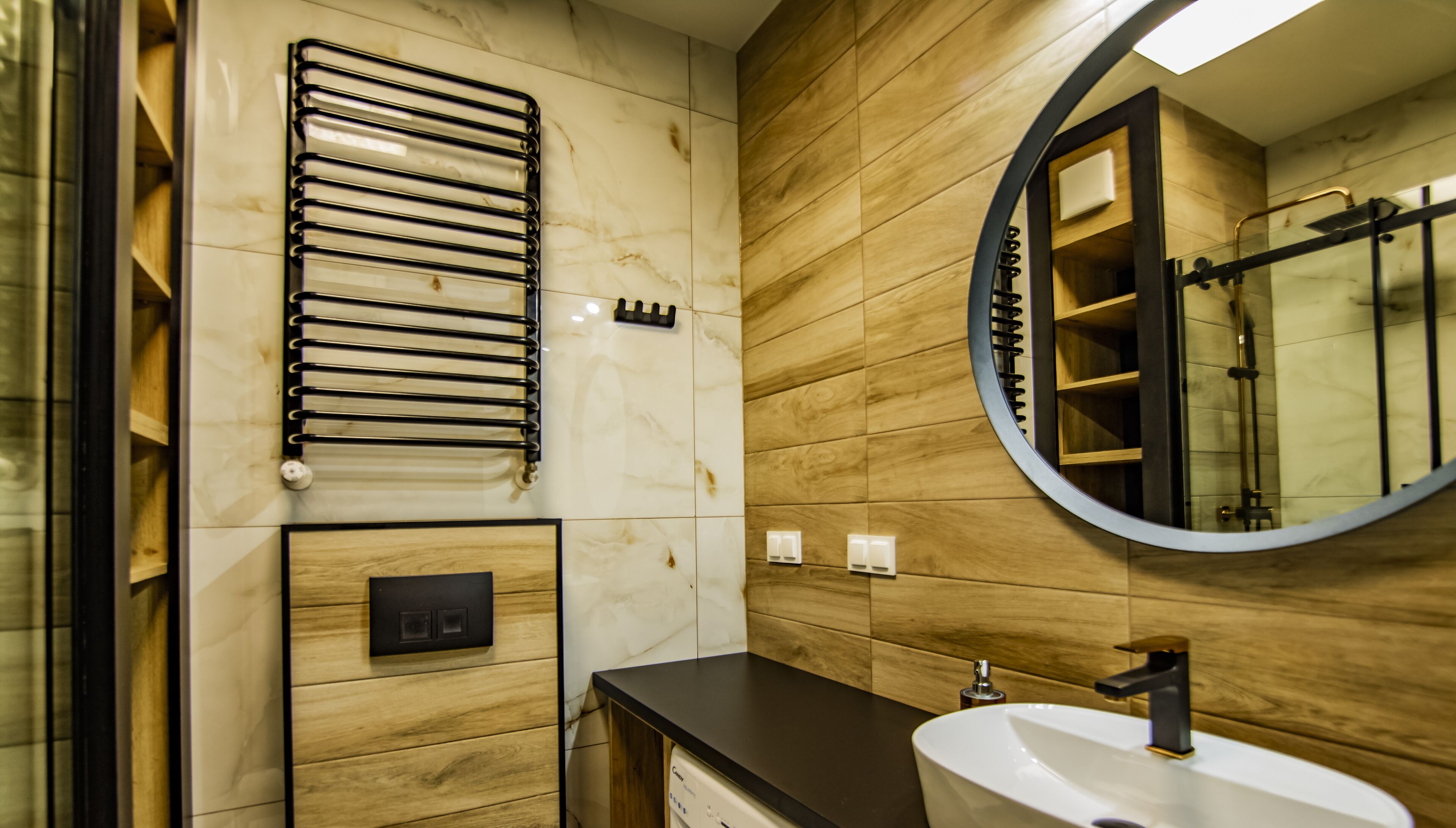 Une salle de bain moderne avec un meuble-lavabo en bois, un lavabo blanc, un miroir rond et un porte-serviettes.
