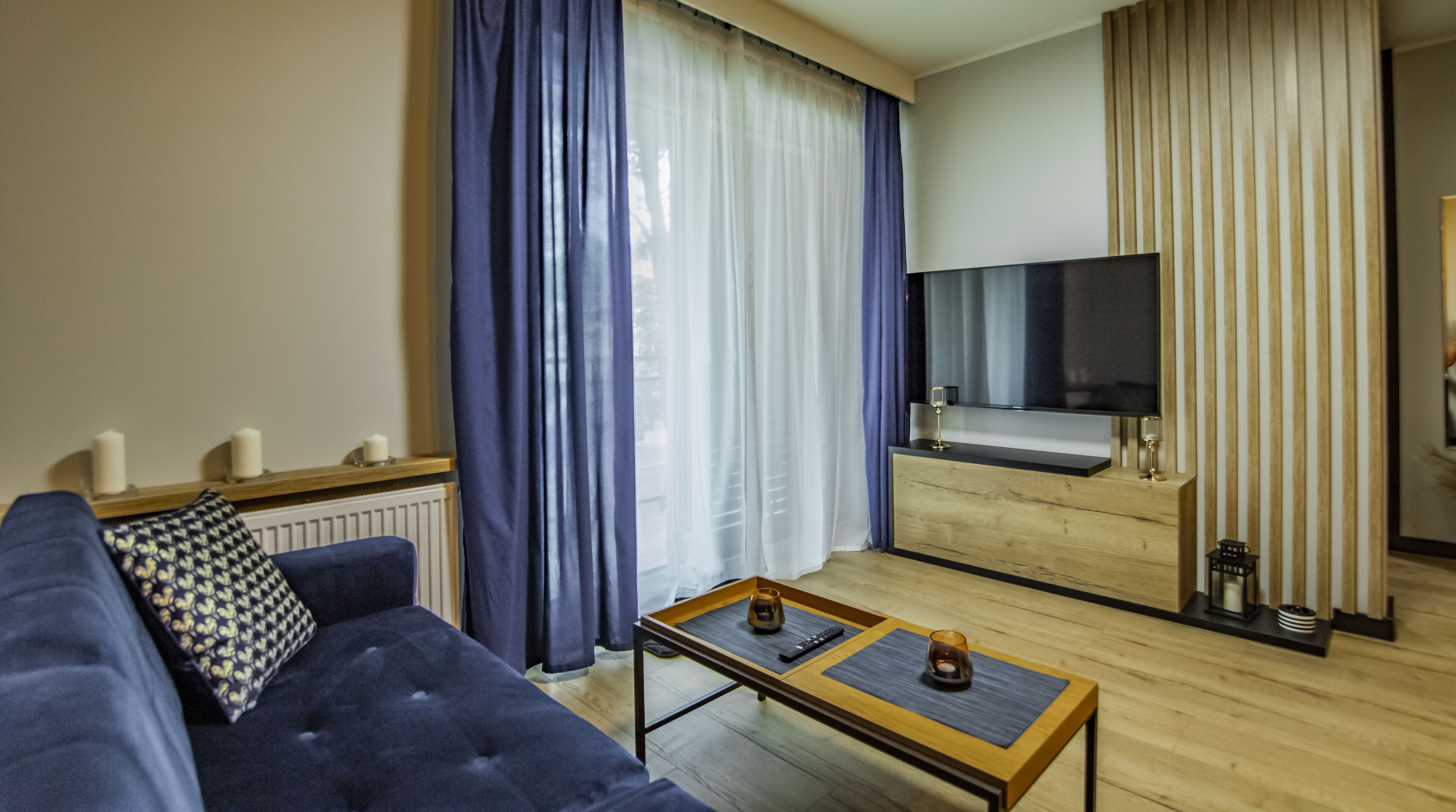 Una sala de estar moderna con un sofá azul, una mesa de centro con controles remotos y un televisor de pantalla plana montado en una pared de madera.