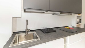 Une cuisine moderne avec un évier en acier inoxydable, des armoires grises et un plan de travail noir.