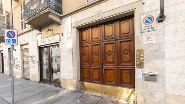 Un bâtiment doté d’une grande porte en bois, d’un panneau indiquant un parking (« P ») et d’un panneau indiquant une zone d’accès pour véhicules (« passo carrabile »).