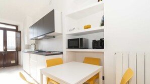 Une cuisine avec des meubles blancs, un four à micro-ondes et une table blanche avec des chaises jaunes.