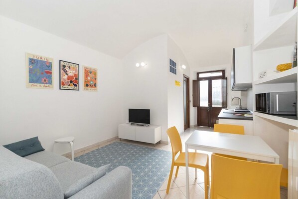 A modern living room with a sofa, a small table, a TV, and a kitchen area with a microwave.