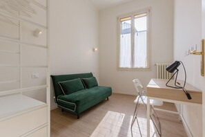 A room with a green sofa, a white desk with a lamp, and a radiator.