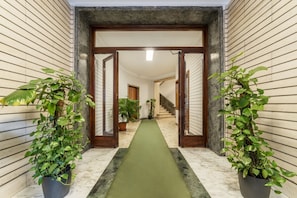 A hallway with a green carpet, wooden walls, and potted plants.