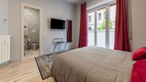 Quarto com cama, televisão, porta deslizante para o banheiro e vista exterior.