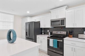 A modern kitchen with white cabinets, a stainless steel refrigerator, a microwave, an oven, and a toaster.