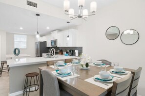 Una cocina moderna con armarios blancos, una isla central y un área de comedor con una mesa de madera dispuesta para cuatro.