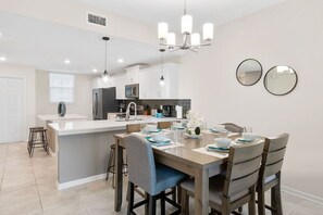 Une cuisine moderne avec des meubles blancs, un îlot central et un coin repas comprenant une table et des chaises en bois.