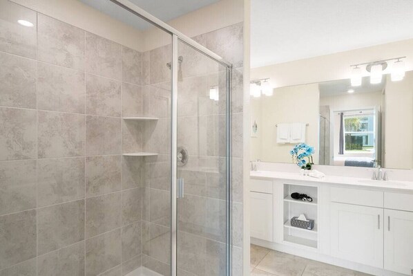 Un baño moderno con ducha envuelta en vidrio, muebles blancos y un espejo grande con luces arriba.