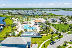 An aerial view of a resort with a central pool, multiple buildings, and a lake.