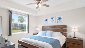 Un dormitorio con una cama, dos mesitas de noche, un ventilador de techo y obras de arte en la pared.