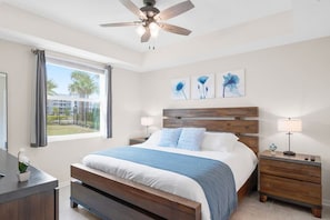 A bedroom with a bed, two bedside tables, a ceiling fan, and artwork on the wall.
