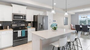 Una cocina moderna con armarios blancos, electrodomésticos de acero inoxidable y una isla central con taburetes de bar.