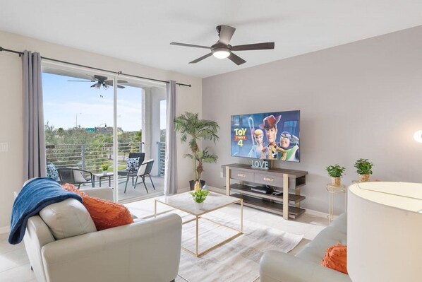 Una sala de estar moderna con un televisor de pantalla plana, un ventilador de techo y un balcón con mobiliario exterior.