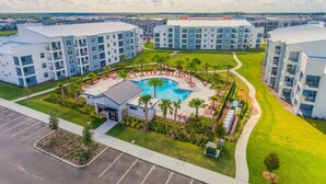 Un moderno complejo de apartamentos con piscina central rodeada de sillones de descanso y palmeras.