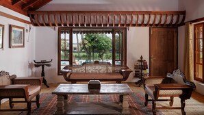 A traditional room with a wooden ceiling, a large window with a view of greenery, a sofa, and a table with a patterned rug.