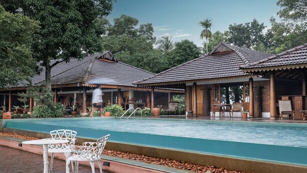 A poolside area with a covered seating area, a pool, and surrounding greenery.