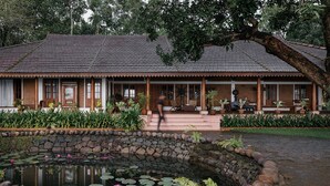 A traditional building with a tiled roof, a stone wall, and a pond with lily pads and water lilies.