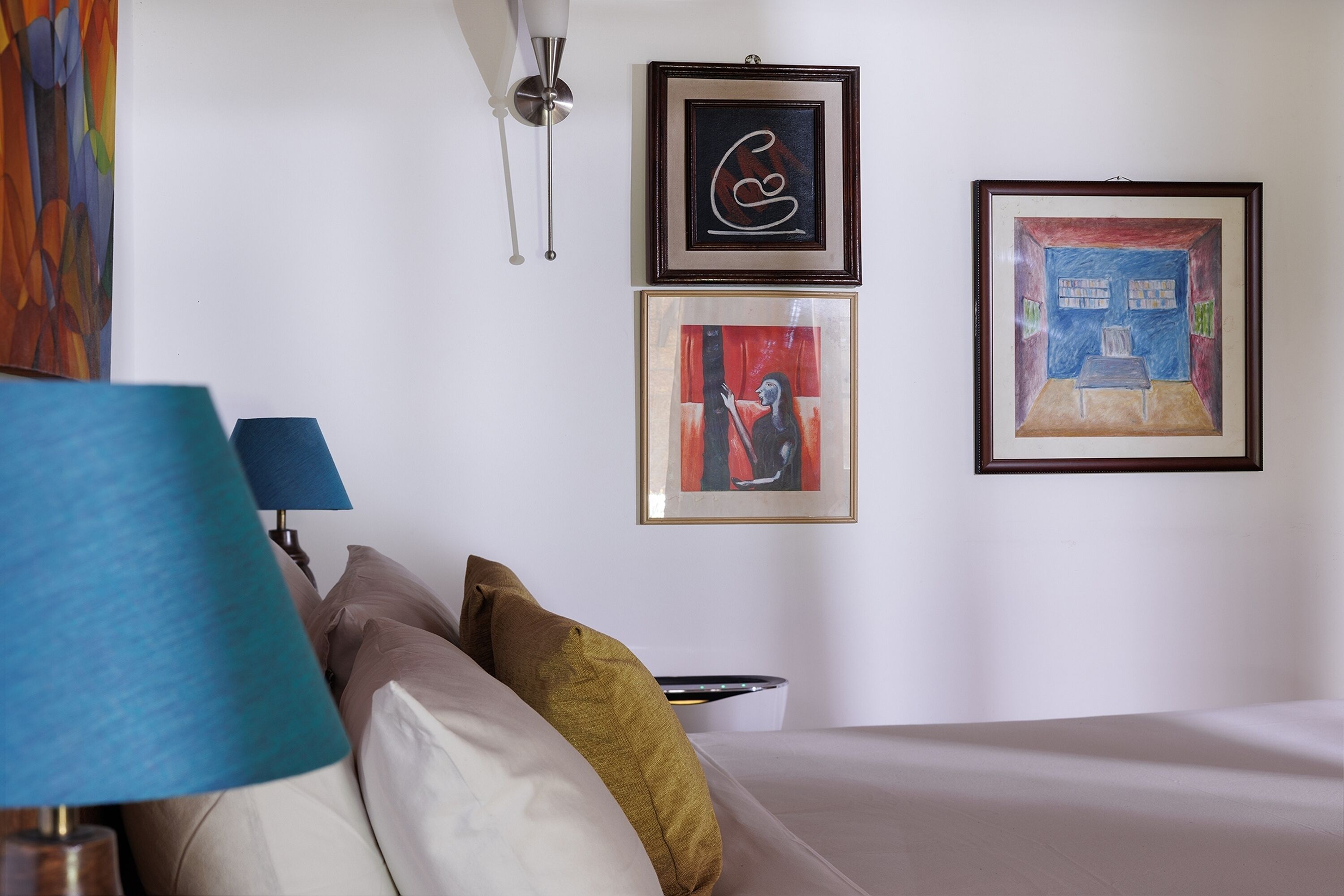 A hotel room with a bed, a bedside table, a lamp, and three framed artworks on the wall.