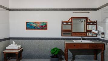Ein Badezimmer mit einem Holzkosmetikschrank, einem Waschbecken, einem Spiegel, einem Handtuchhalter, einer Topfpflanze und einem farbenfrohen abstrakten Gemälde an der Wand.