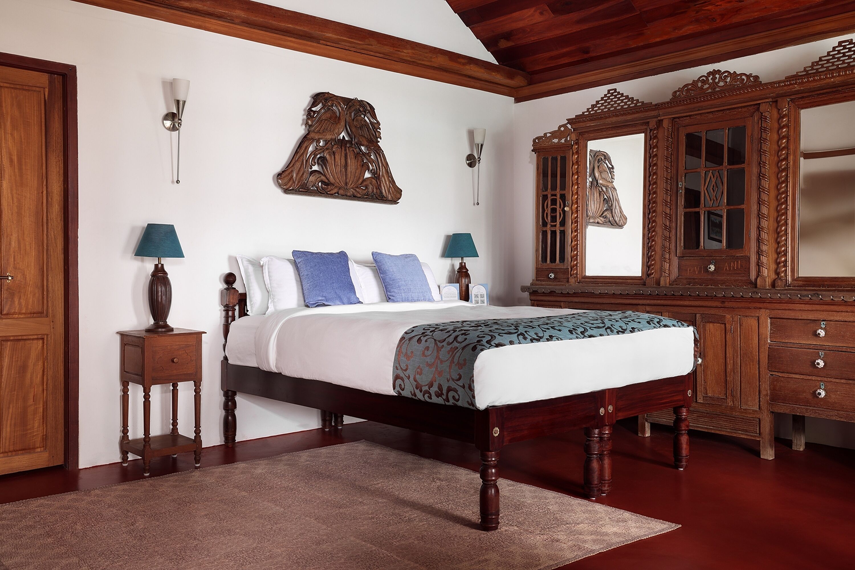 A bedroom with a wooden bed, two bedside tables with lamps, a large mirror, and a wooden wardrobe.