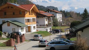 A row of traditional wooden houses with sloped roofs, a paved driveway, and a mountain backdrop.