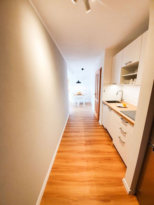 A narrow hallway with wooden flooring leading to a kitchen area with white cabinets and a sink.