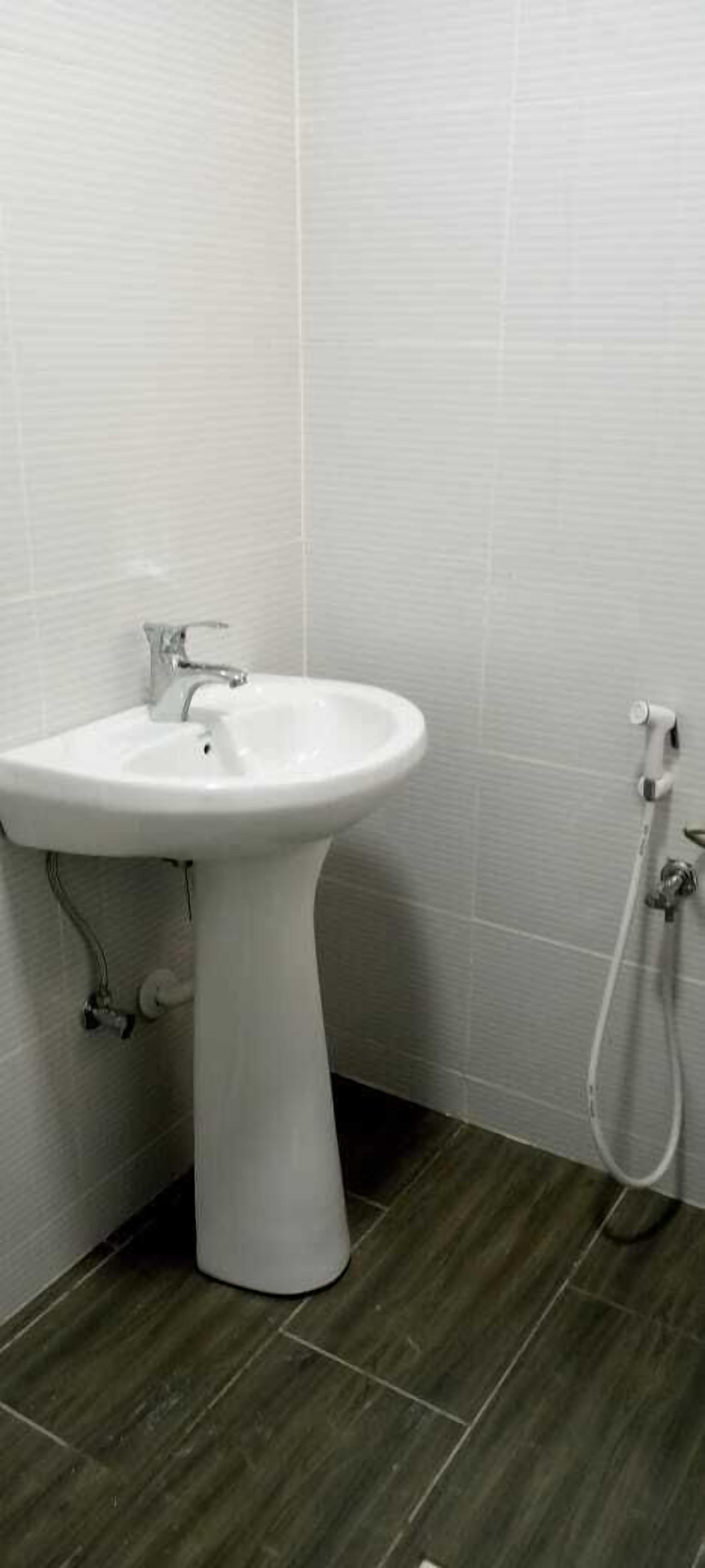 A white pedestal sink with a faucet and a handheld showerhead against a tiled wall.