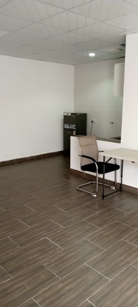 Una habitación con piso de madera oscura, pared blanca y una silla de oficina negra.
