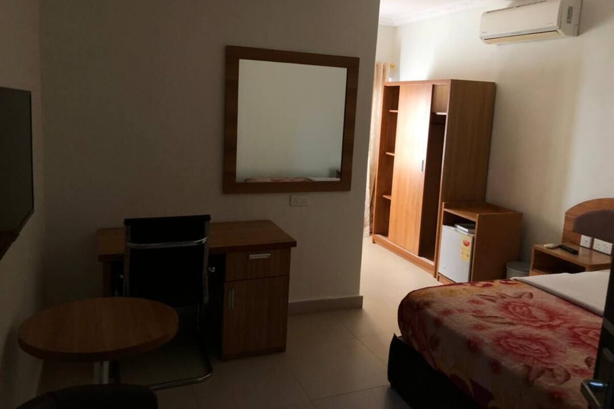 A hotel room with a bed, a desk, a chair, a wardrobe, and a mirror.