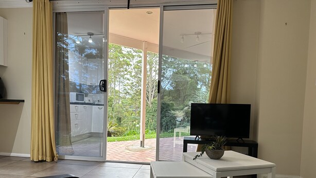 A room with a sliding glass door leading to a garden, a white table with a plant, and a black sofa.